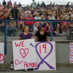 FILE - Donna Chamblee, front left, and Nicole Fought, front right, hold signs July 2, 2013, on the football field at Prescott High School in Prescott, Ariz., during a vigil for 19 firefighters killed June 30, 2013, while battling the Yarnell Hill Fire. Friday, June 30, 2023, marks 10 years since one of the deadliest wildland fires in the U.S. killed 19 members of an elite central Arizona crew. The city of Prescott and neighboring town of Yarnell, Ariz., are honoring the Granite Mountain Hotshots with public events, including 19 bell tolls.
