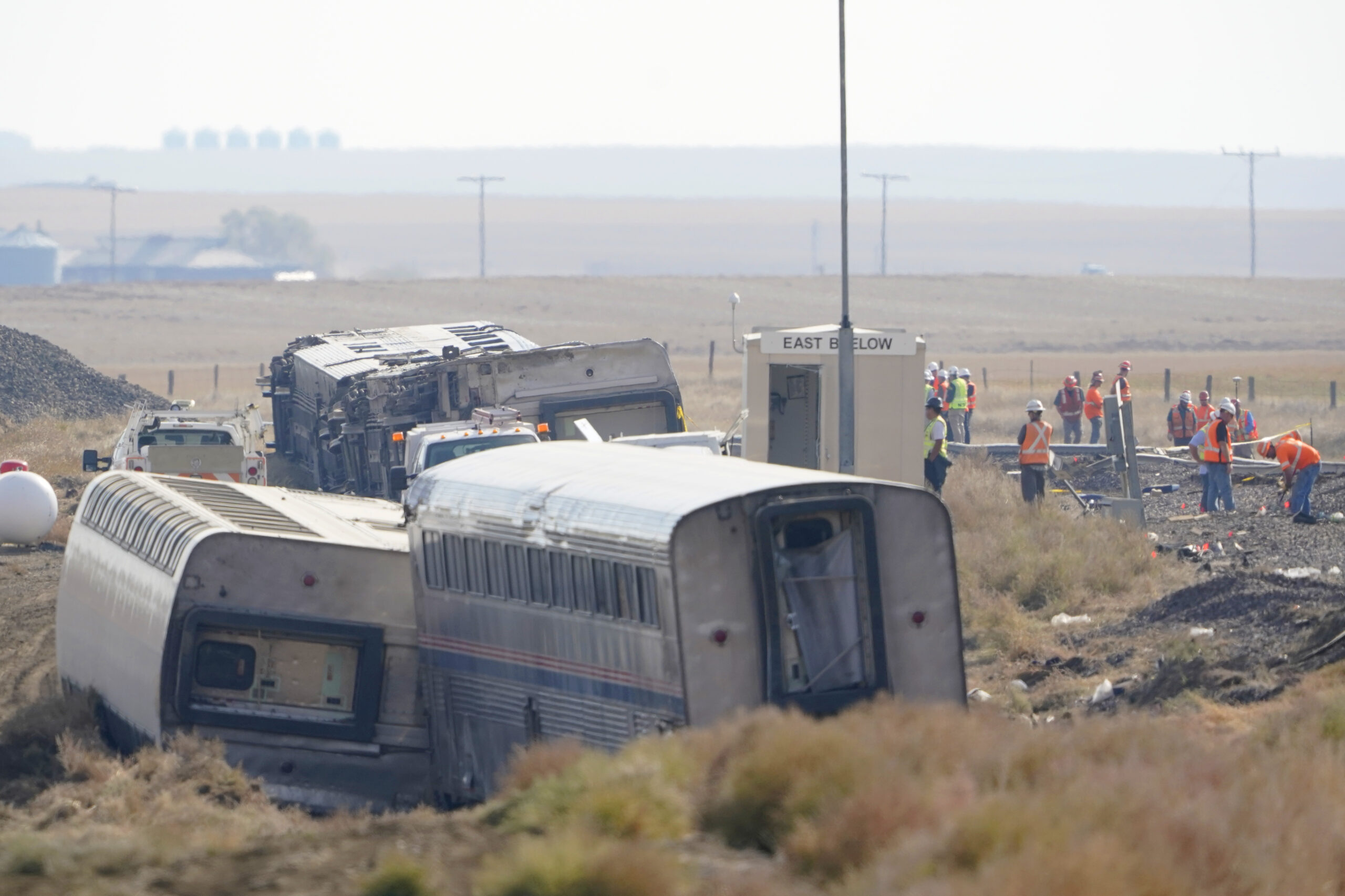 FILE - Workers stand near train tracks, Sept. 27, 2021, next to overturned cars from an Amtrak trai...
