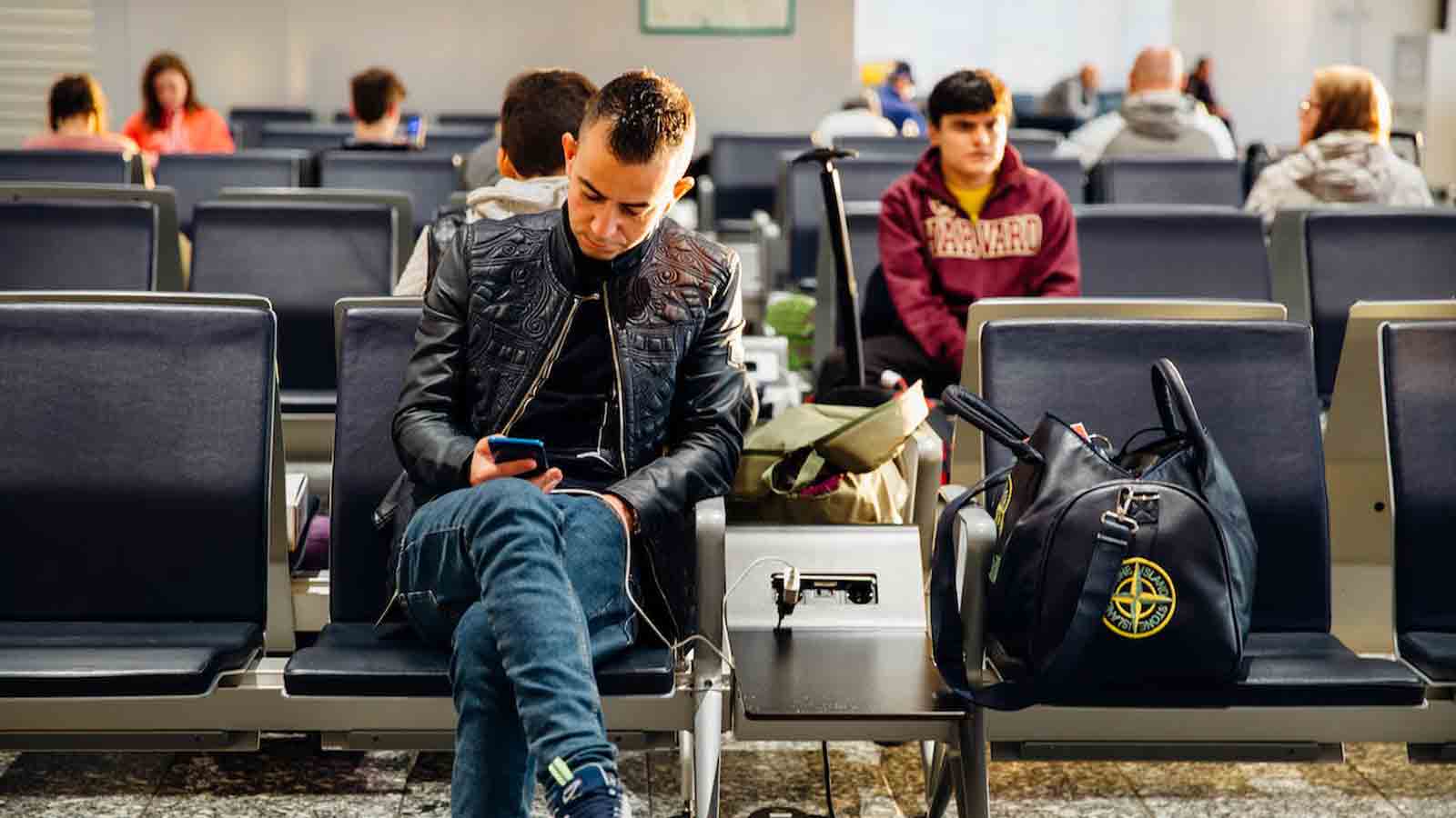 Man sits in airport chair as he charges his cellphone....