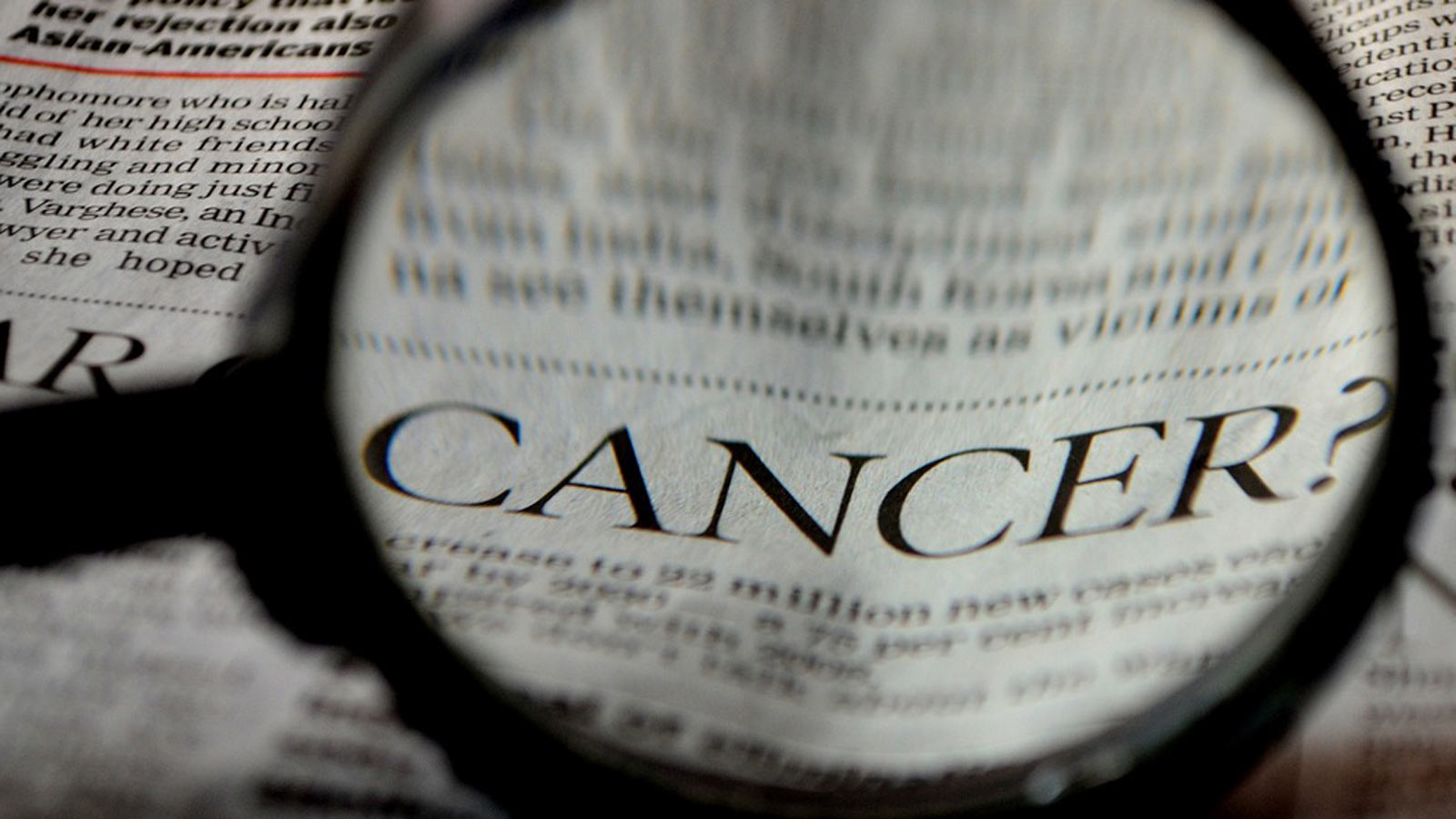 A magnifying glass enlarges the word "cancer" on a newspaper...