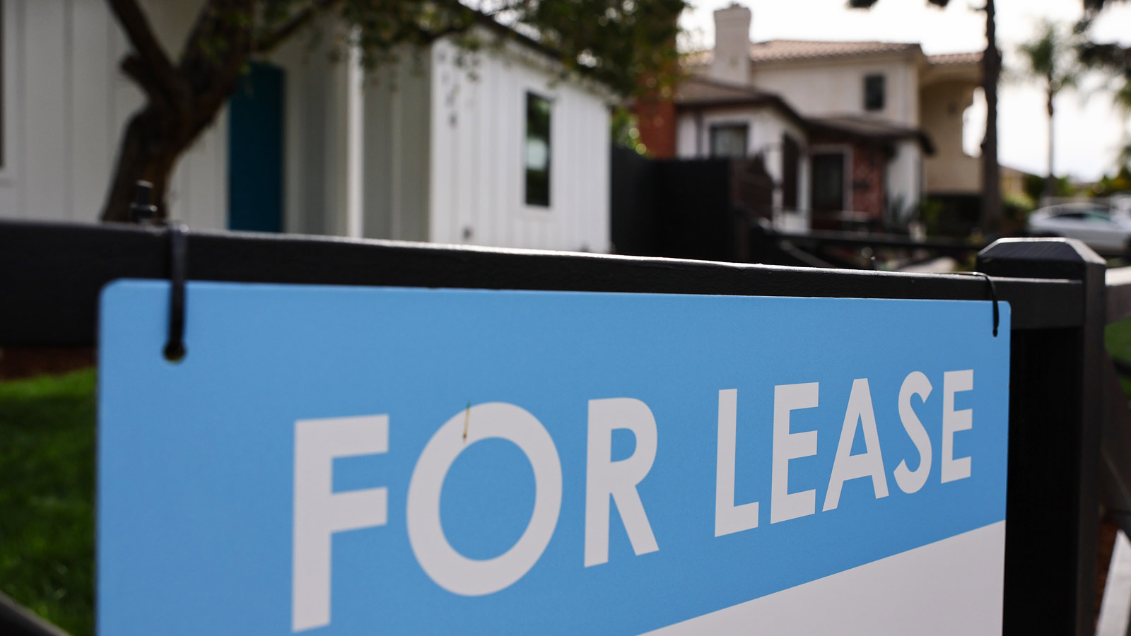 A sign reading "for lease" is seen in the foreground with a house behind it...