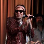 Rapper Yelawolf smiles while holding a microphone. He will perform at Arizona Bike Week 2024.
