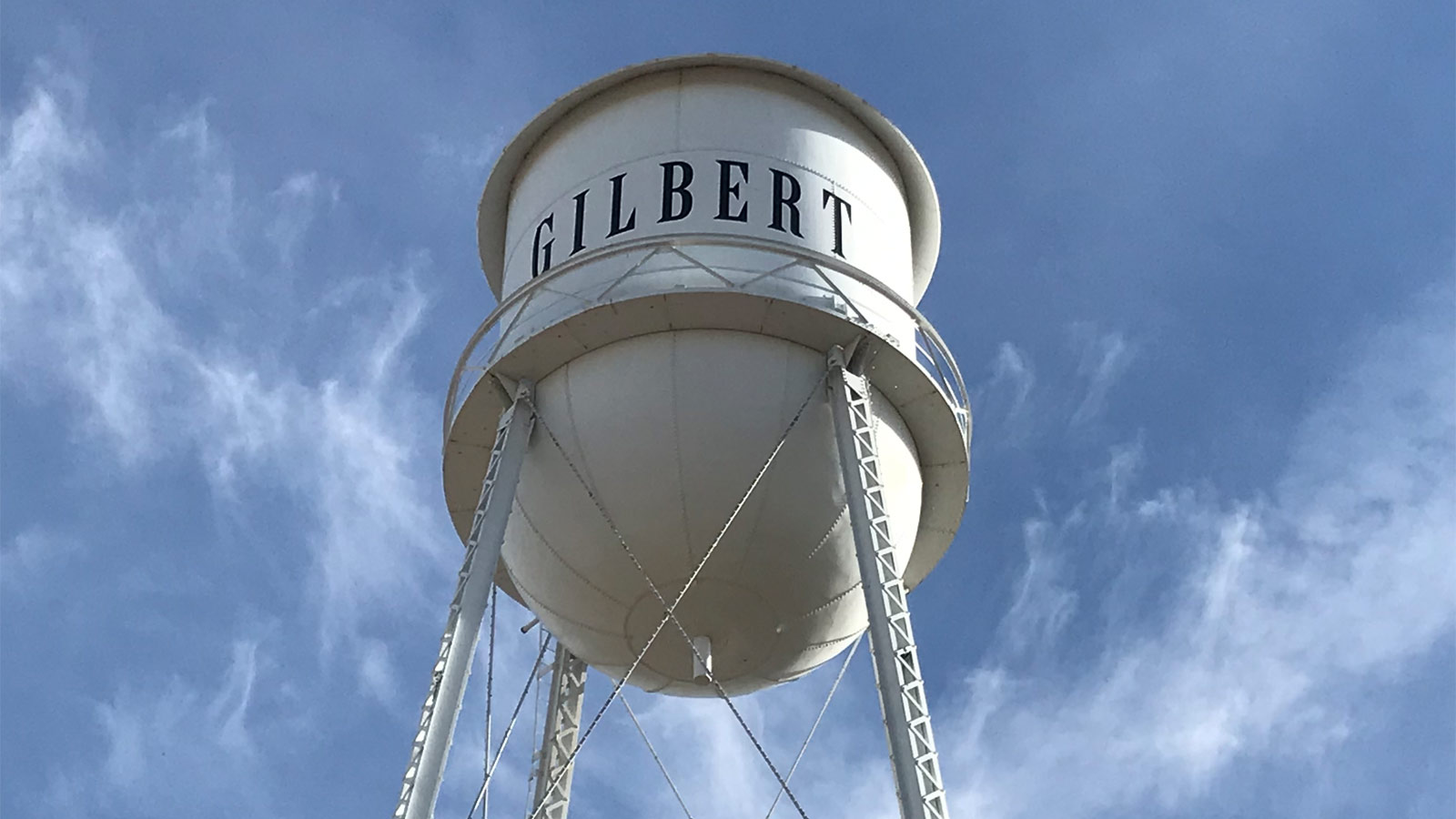 A view of the Gilbert water tower from below, with wispy clouds in the blue sky behind it....