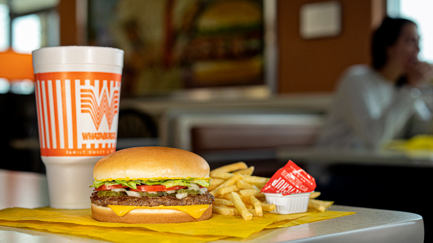 A promotional photo shows a drink in an orange and white cup with a hamburger and fries on a table ...