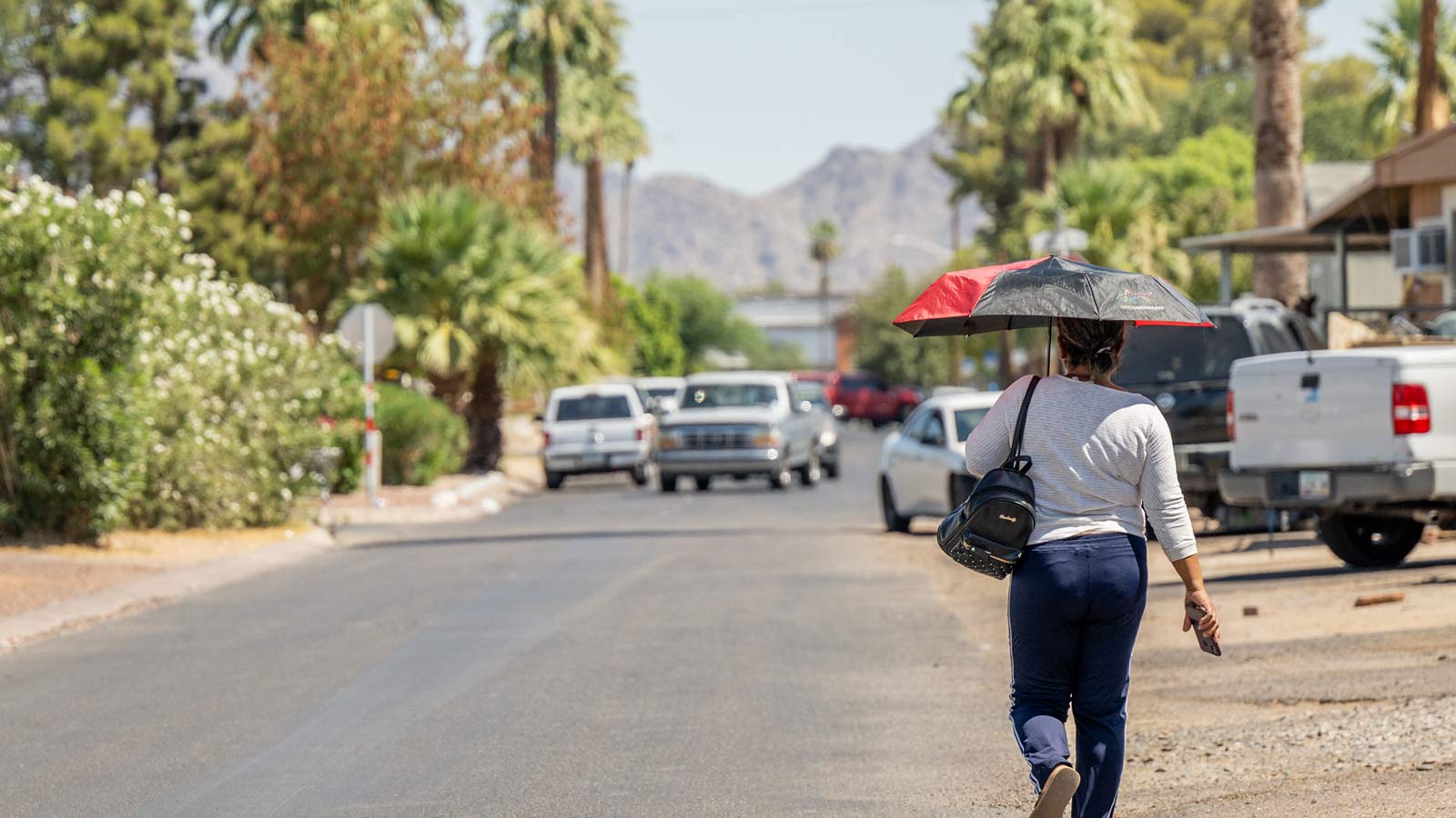 A woman uses an umbrella to shield herself from the sun while walking in Phoenix in the summer of 2...