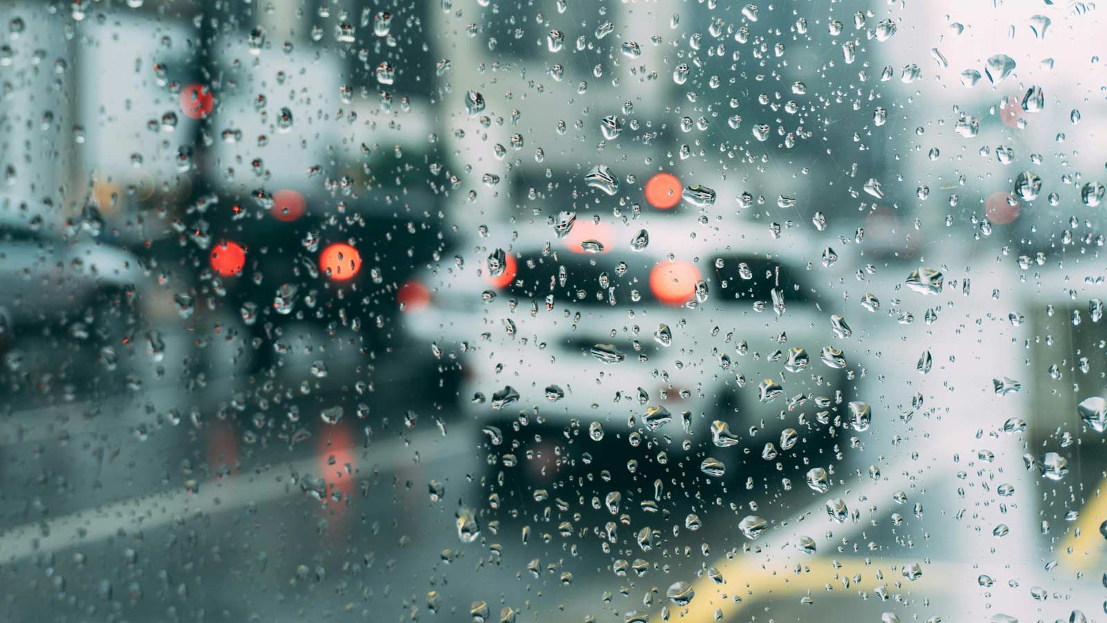 Cars are seen driving on a wet street through drops on a window or windshield on a rainy day....