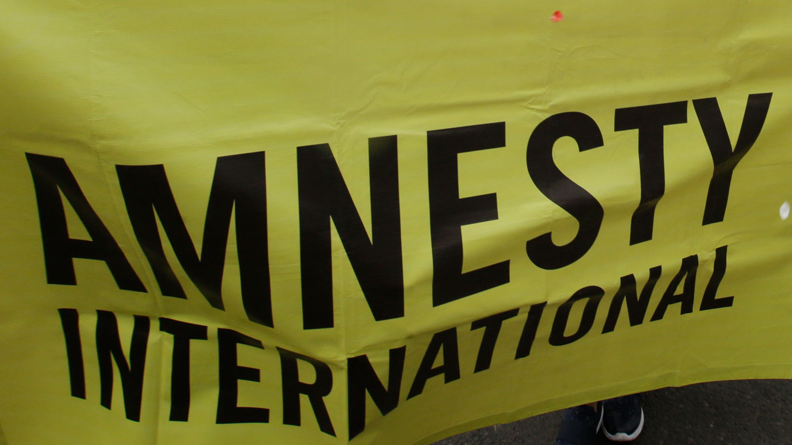 A yellow banner with black writing says Amnesty International. The group has been accused of promot...
