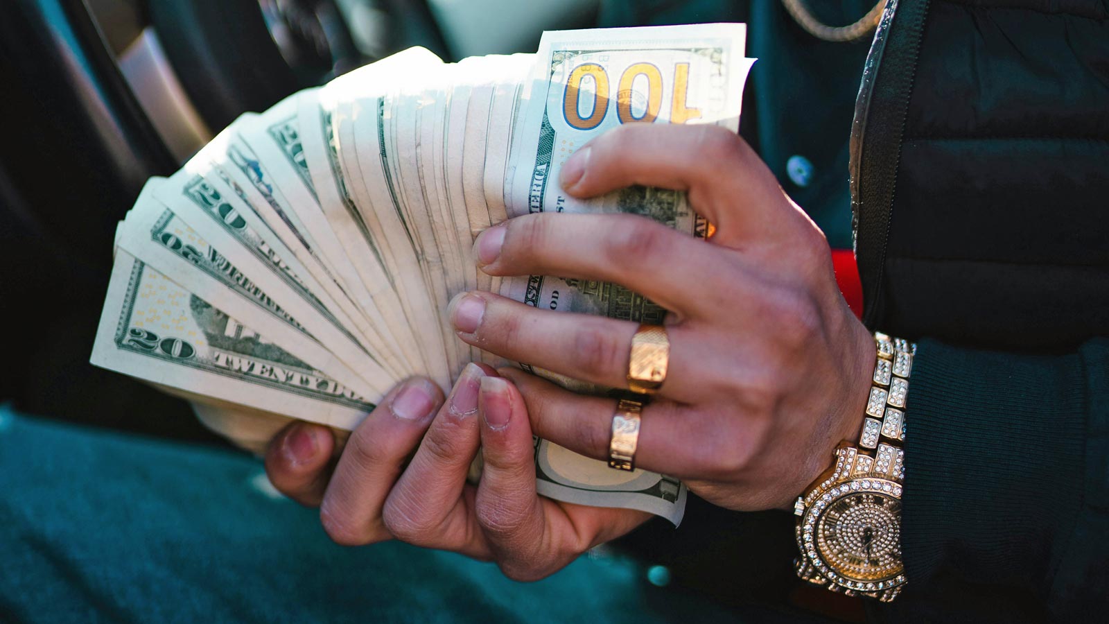 A person wearing flashy rings and a watch fans out a big stack of cash bills....