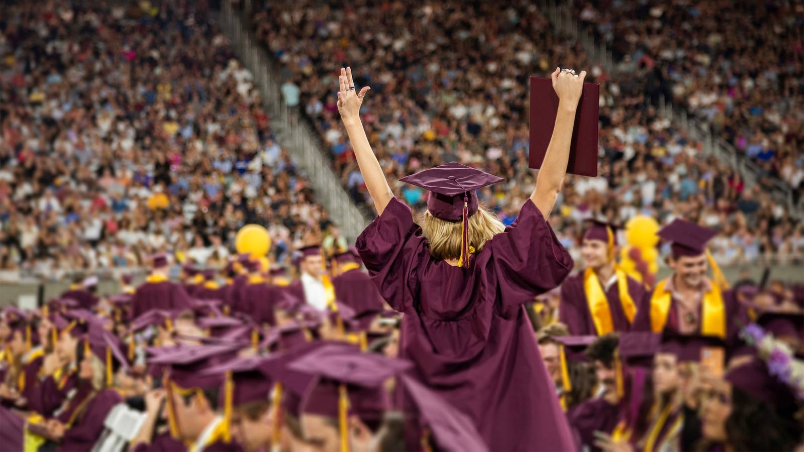 An Arizona State University graduate raises her arms amid a sea of maroon robes during an undated g...
