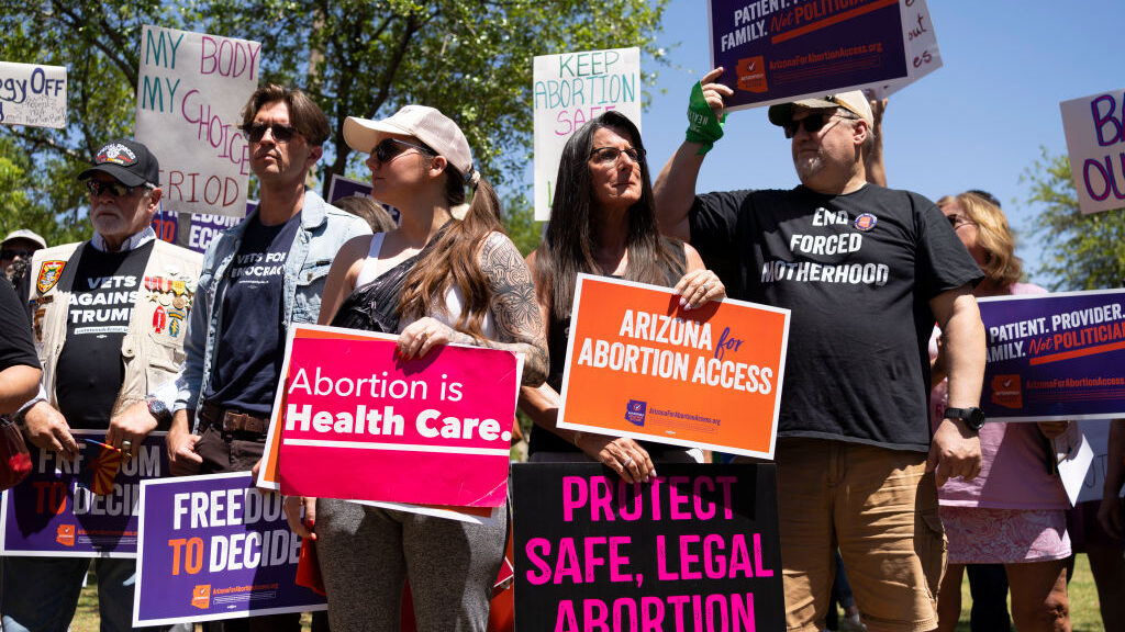 Pro-choice protestors stand outside with colorful signs. They read "Arizona for Abortion Access," "...