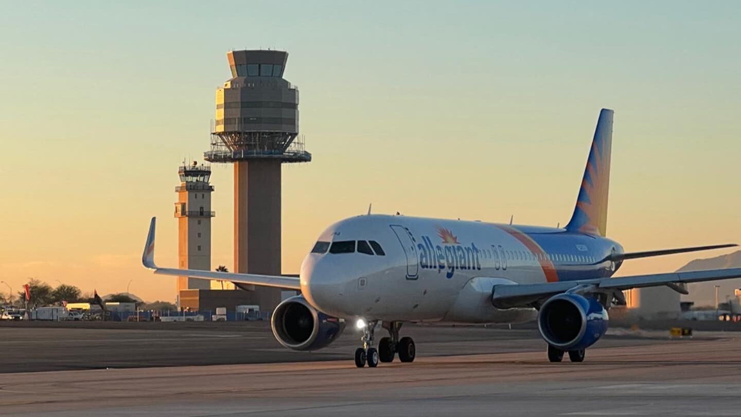 A plane on a runway with an air traffic control tower in the background against a sunset....