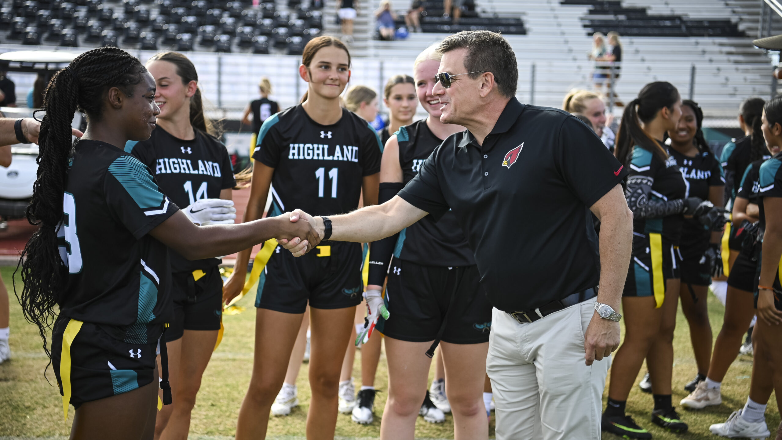 Michael Bidwill shakes hands with a female athlete in flag football gear...