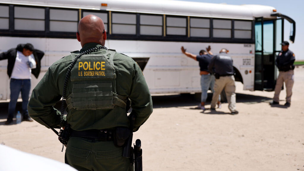 Border Patrol agent looks at immigrants being detained near a bus....