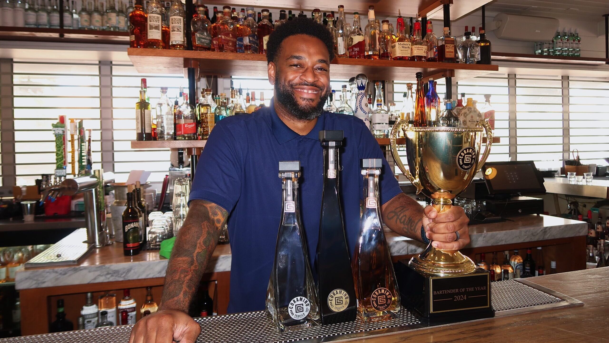 A man smiles while he stands behind a bar. He holds a trophy....