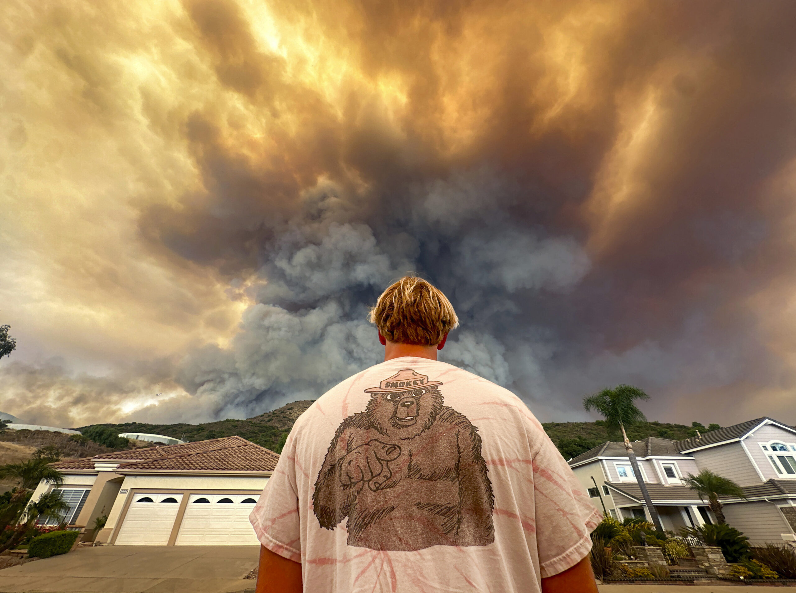 Aidan Thomas wears a Smokey Bear t-shirt as he watches smoke from the Airport Fire rise behind Mean...