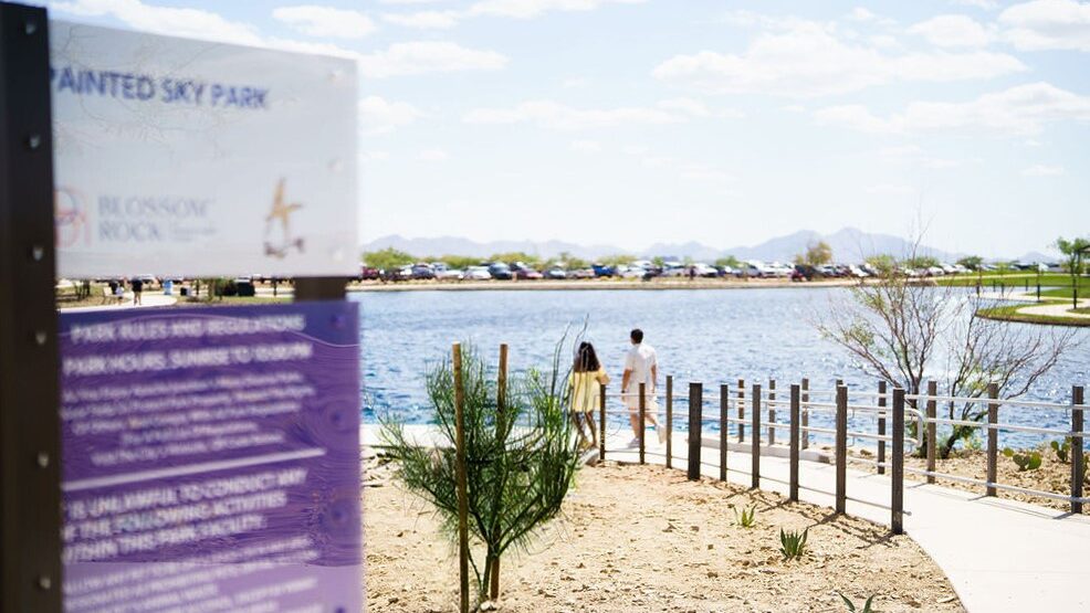 Painted Sky Park sign and view of two people walking on sidewalk beside lake...