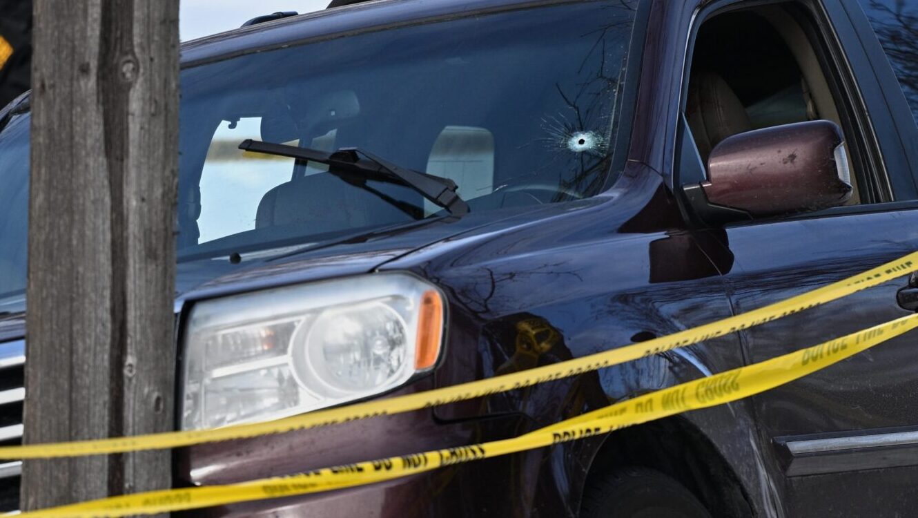 A bullet hole is seen in the windshield as law enforcement officers work at the scene of a shooting...