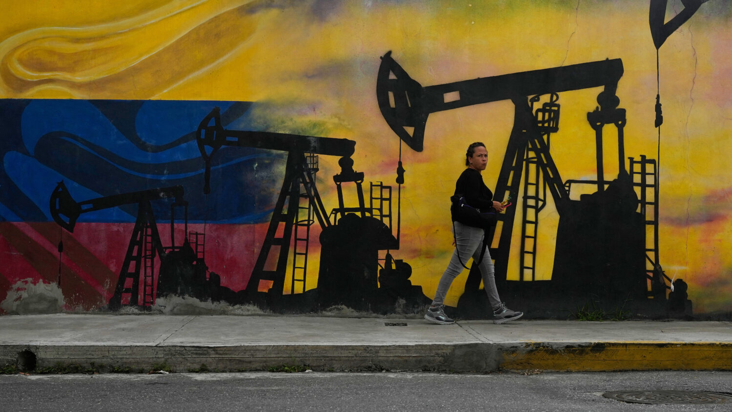 A local walks past a mural featuring oil pumps and wells in Caracas, Venezuela, Tuesday, Jan. 6, 20...