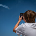 A young attendee captures a photo of the U.S. Air Force Thunderbirds as they perform a high-altitude maneuver during Luke Days 2024 at Luke Air Force Base, Ariz., on March 22, 2024. The air show attracted thousands of spectators, providing a firsthand experience of military aviation. (U.S. Air Force photo by Tech. Sgt. Tyler J. Bolken)