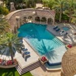 A resort style pool serves as the centerpiece of the outdoor living space, complete with a swim up bar, ramada, and multiple entertainment zones.