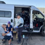 A Circle the City medical worker examines a patient outside the nonprofit's mobile unit at a Phoenix park. The city is considering an ordinance that would require permits for medical treatment in parks. (Credit: Balin Overstolz-McNair)