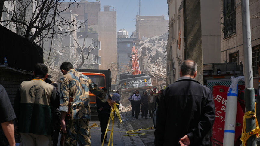 Bystanders watch from a distance as rescue teams and first responders work at the site of a strike ...