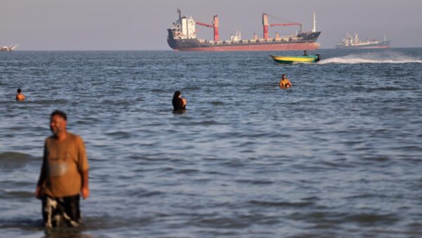 Residents swim in the waters of the Strait of Hormuz as a small motorboat passes cargo ships and other commercial vessels offshore near Bandar Abbas, Iran, Wednesday, June 17, 2026. (Amirhosein Khorgooi/ISNA via AP)