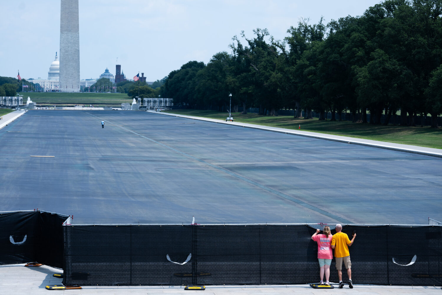 Individuals peek over the fence to see the drained Lincoln Memorial Reflecting Pool,, Monday, July ...