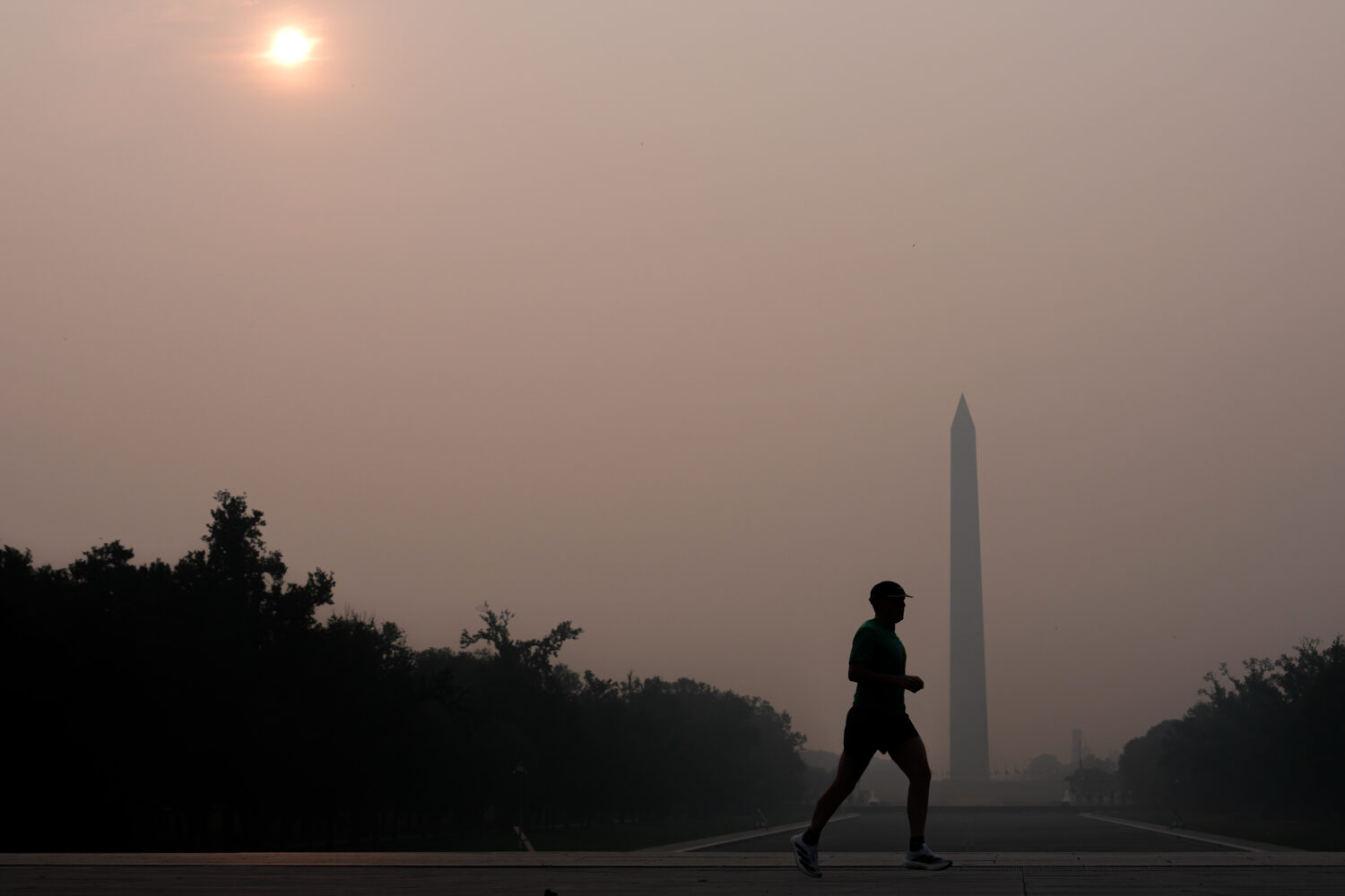 The sun is obscured by wildfire smoke as a person runs in front of the Washington Monument and Linc...