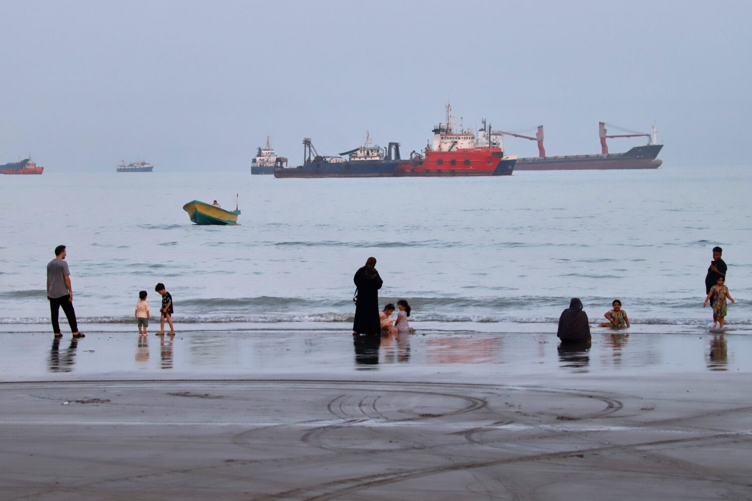 People spend time at a beach as commercial vessels are anchored in the Strait of Hormuz off Bandar ...