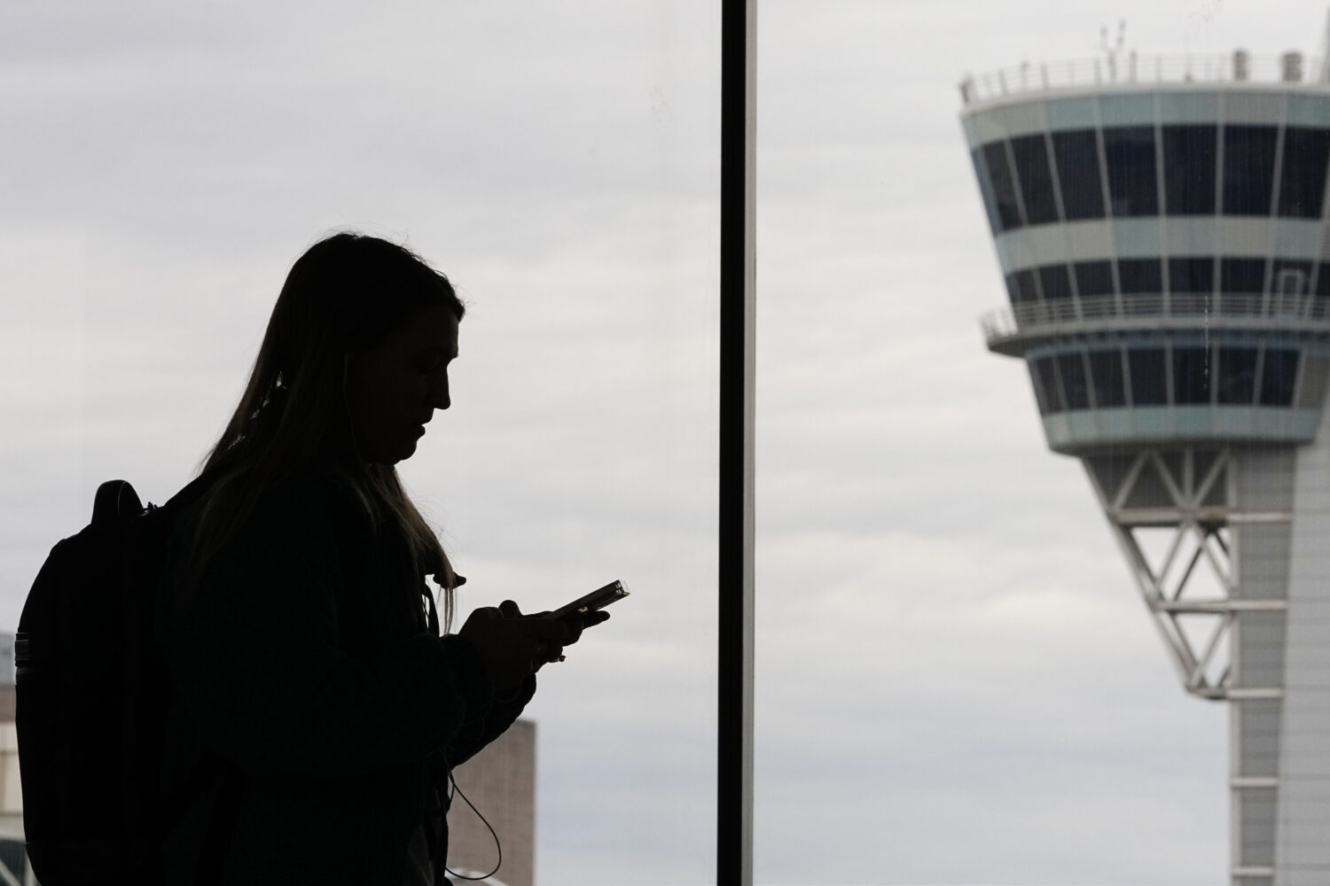 FILE - A traveler with a smartphone walks past an air traffic control tower at Philadelphia Interna...