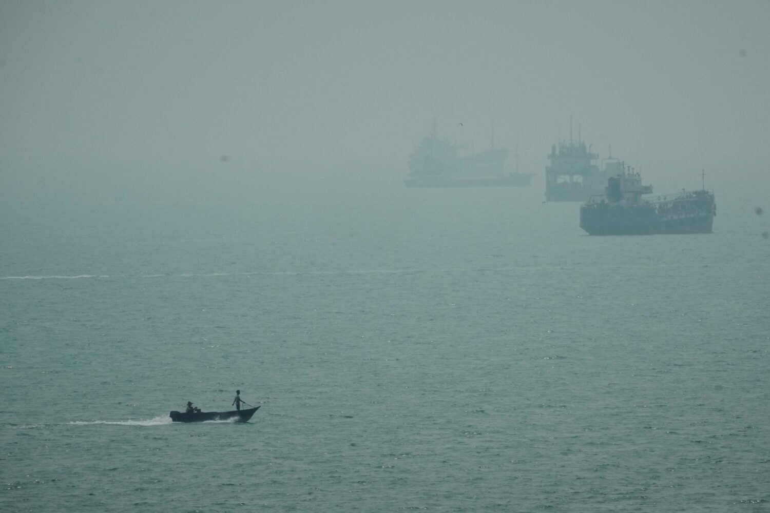 FILE - A motorboat travels past commercial vessels anchored amid haze in the Strait of Hormuz off B...