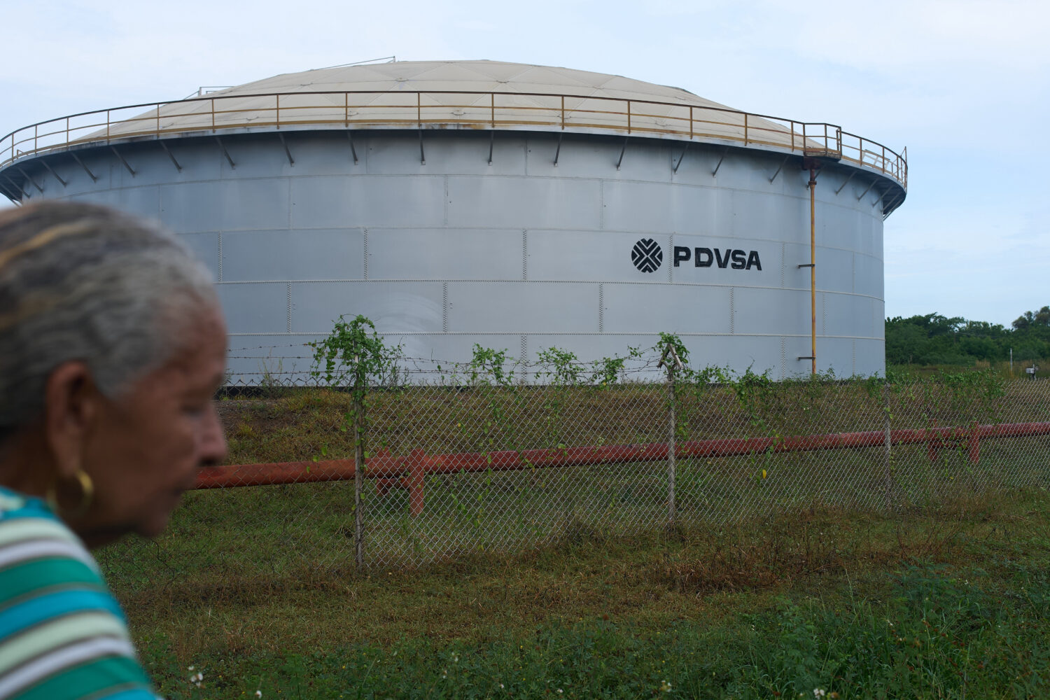 A woman walks near of a oil storage tank of Venezuela's state-run oil company, PDVSA in Cabimas, Ve...