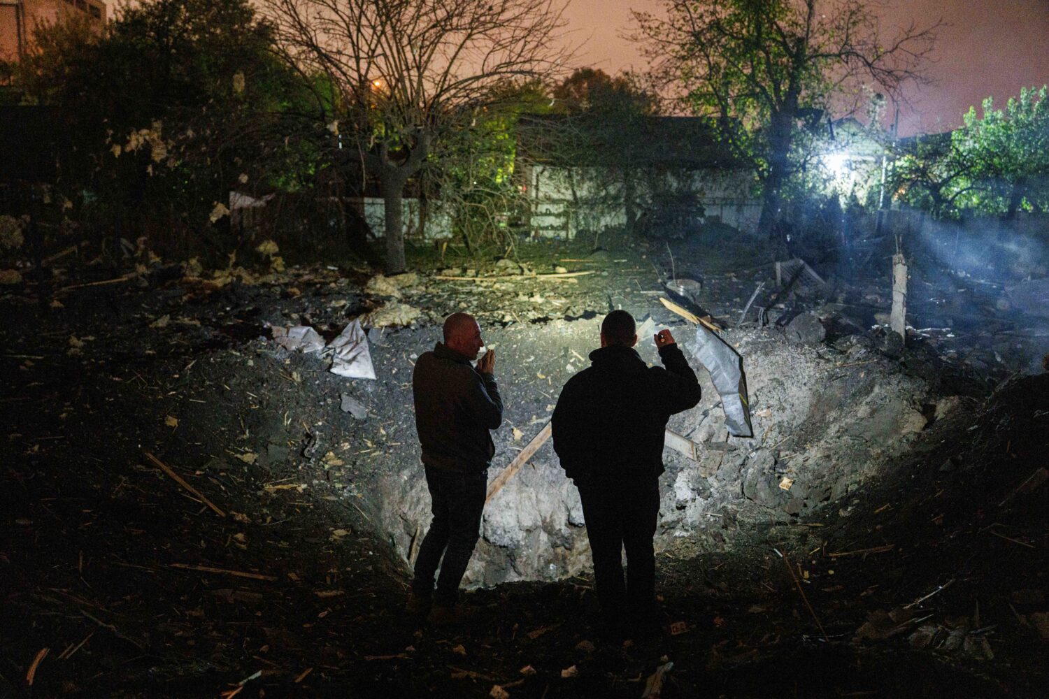 People look at a crater after a Russian missile strike in a residential neighborhood in Kyiv, Ukrai...