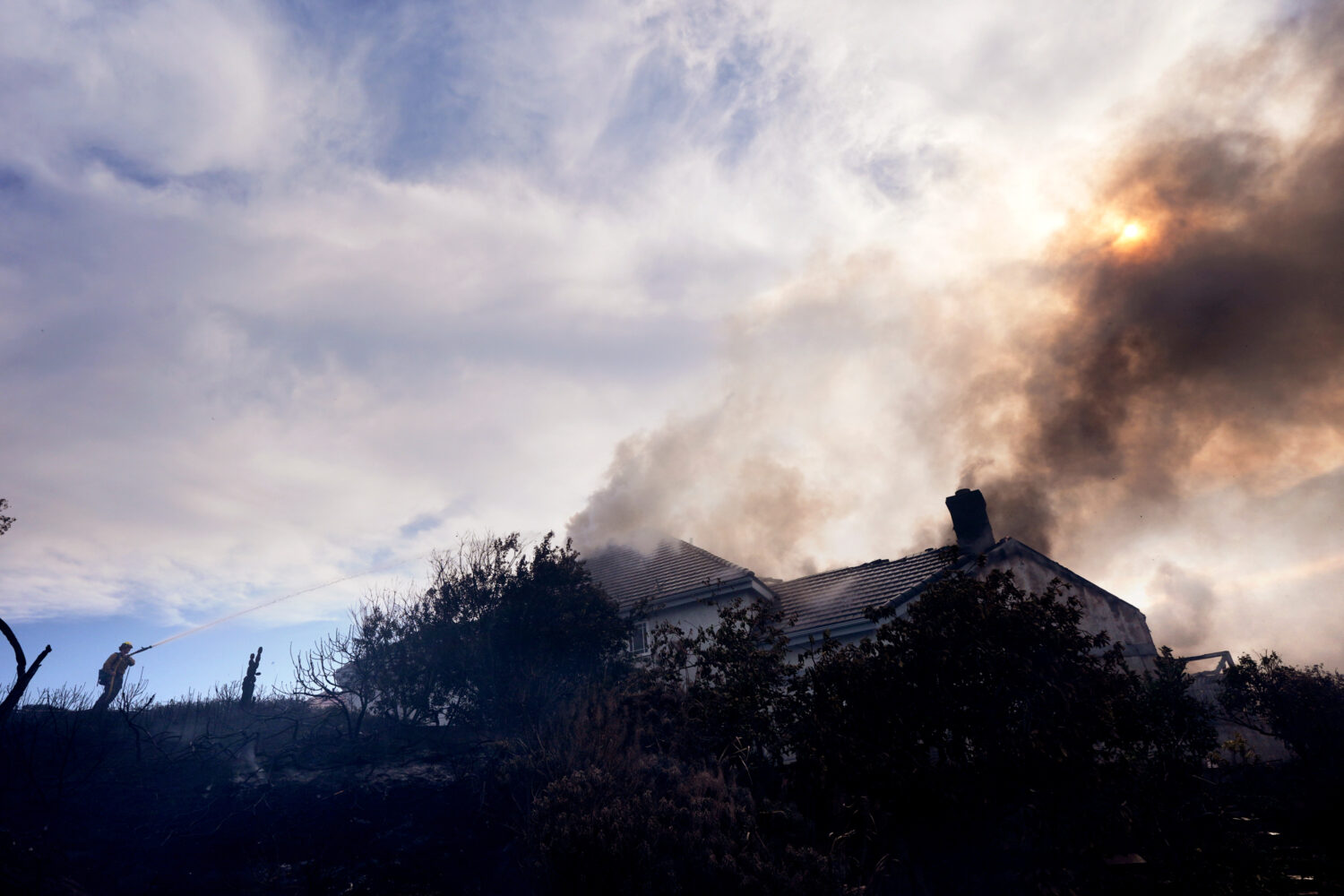 A firefighters works to put out a fire on a house engulfed in flames during the Norte Fire on Frida...