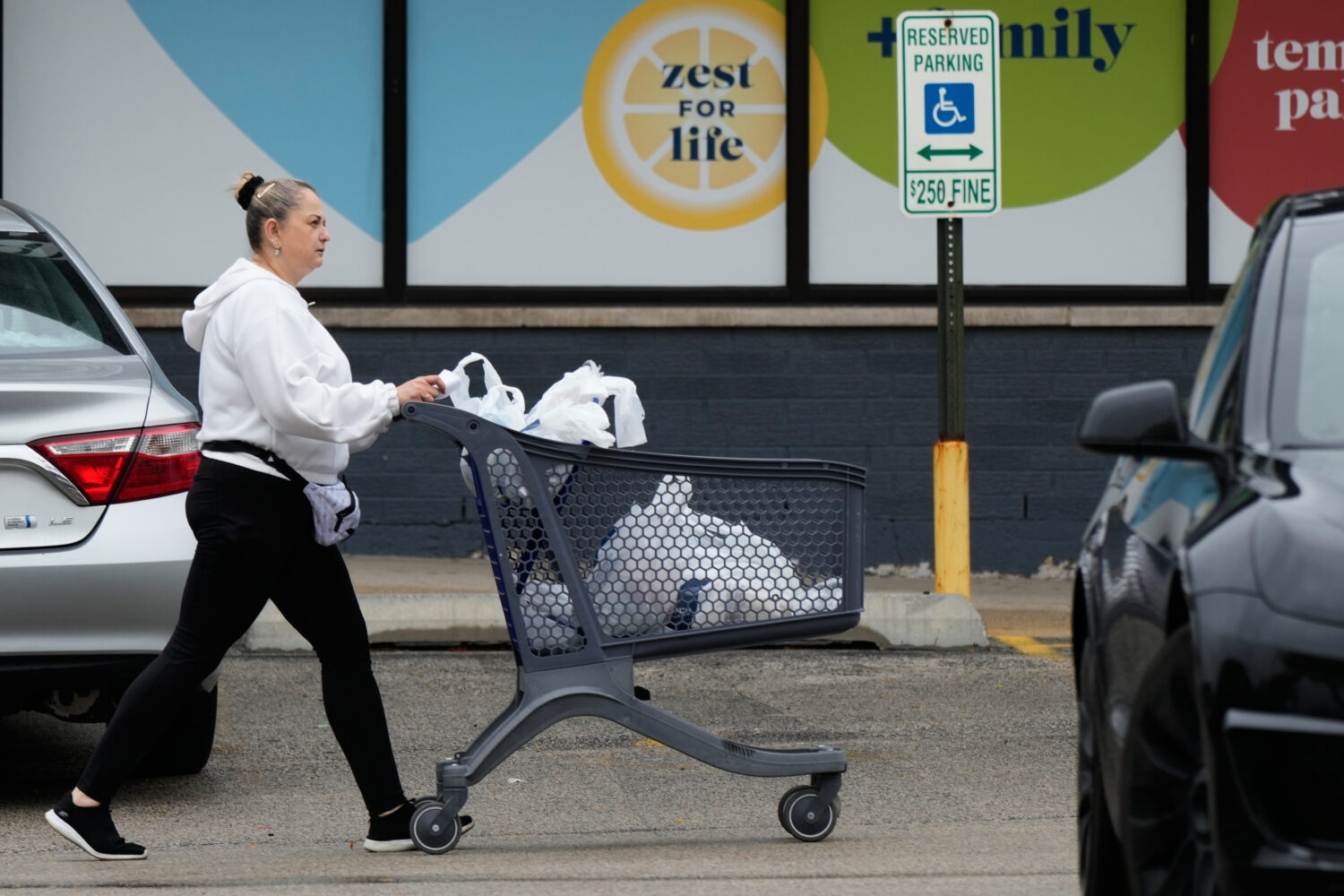 A woman pushes a shopping cart as she leaves a grocery store in Arlington Heights, Ill., Wednesday,...
