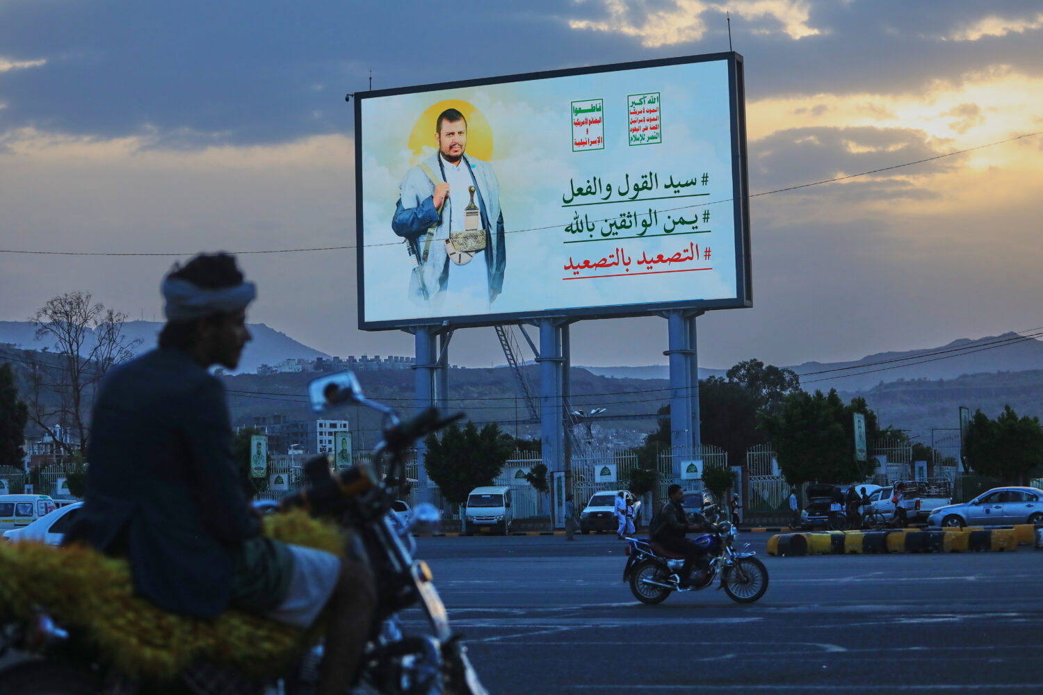 People ride their motorbikes under a billboard showing Houthi leader Abdul Malik al-Houthi with a p...