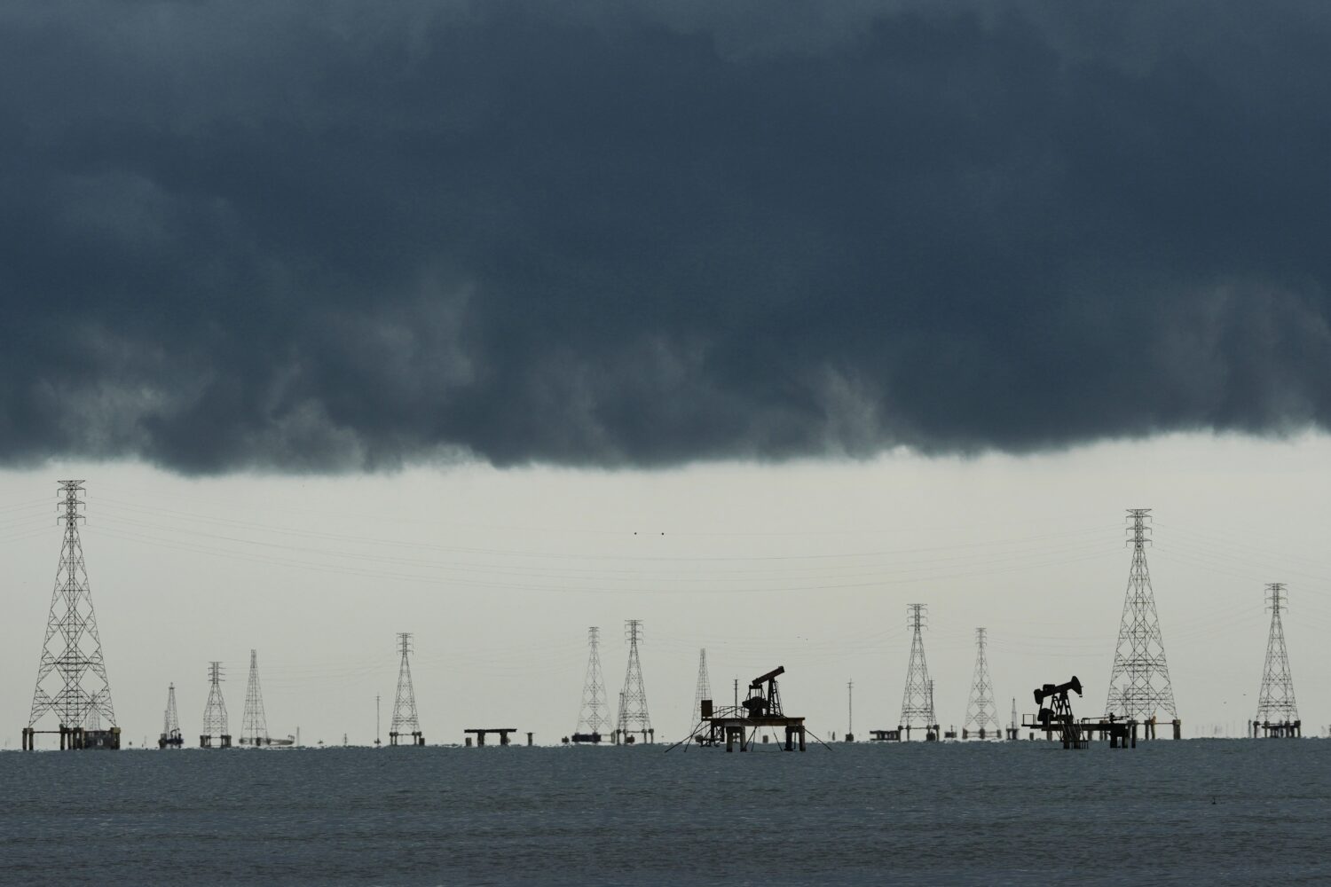FILE - Clouds form over pumpjacks and power transmission towers on Lake Maracaibo in Cabimas, Venez...