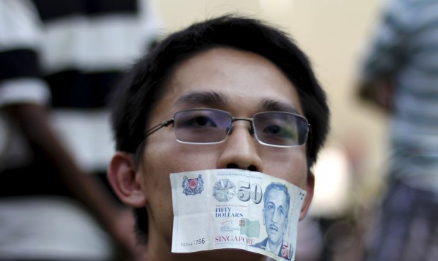 In this June 8, 2013, file photo, a man covers his mouth with a fifty dollar bill to represent the ...