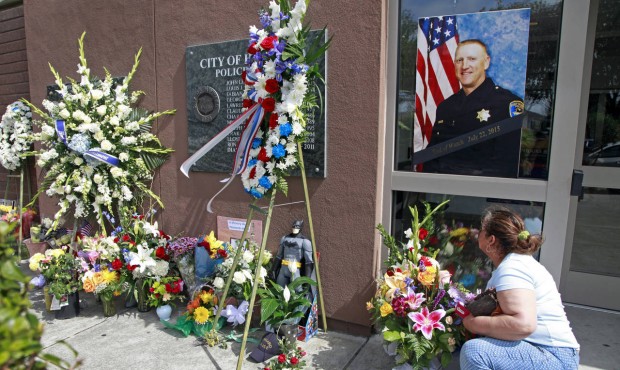n Hayward resident Hilda Sierra moves some flowers under the portrait of fallen Sgt. Scott Lunger o...