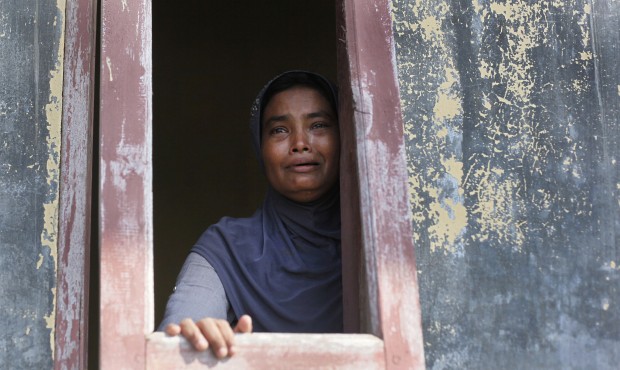 An ethnic Rohingya woman weeps as she looks outside from a window at a temporary shelter for the mi...