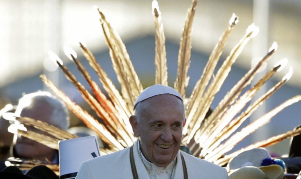 n Pope Francis is framed by a feather headdress worn by one of the indigenous people and children w...