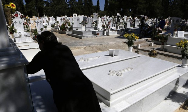 A woman lights a candle on a grave at a cemetery in Athens, Friday, July 17, 2015. Funeral homes he...