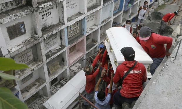 Workers slides the coffin of one of the fire victims into apartment type-crypts during a mass inter...