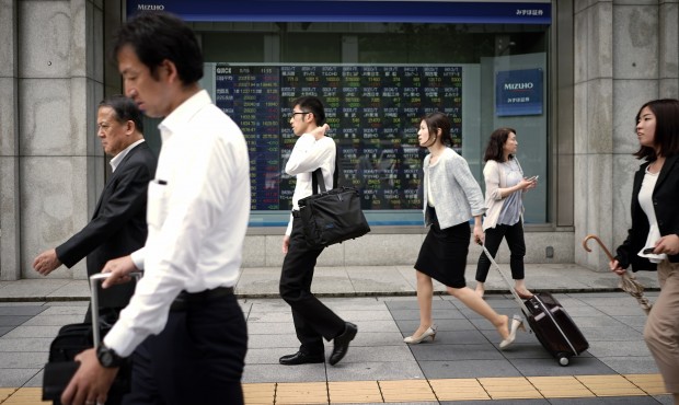 People walk past an electronic stock board of a securities firm in Tokyo, Tuesday, May 19, 2015. As...