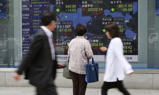 People look at an electronic stock board of a securities firm in Tokyo, Monday, June 22, 2015. Stoc...