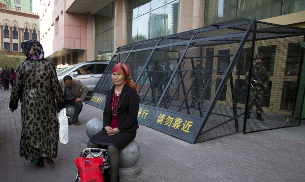 FILE – In this May 1, 2014 file photo, a Uighur woman rests near a cage protecting heavily ar...