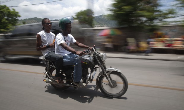 In this May 21, 2015 photo, Joseph Marc Carel, a motorcycle taxi driver, takes a passenger to downt...