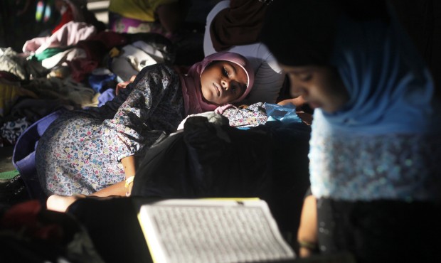 An ethnic Rohingya woman rests on a pile of used clothing donated by local residents as another rea...