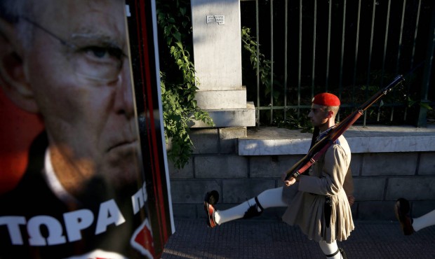 An Evzone of the presidential guard passes by a poster of German Finance Minister Wolfgang Schaeubl...